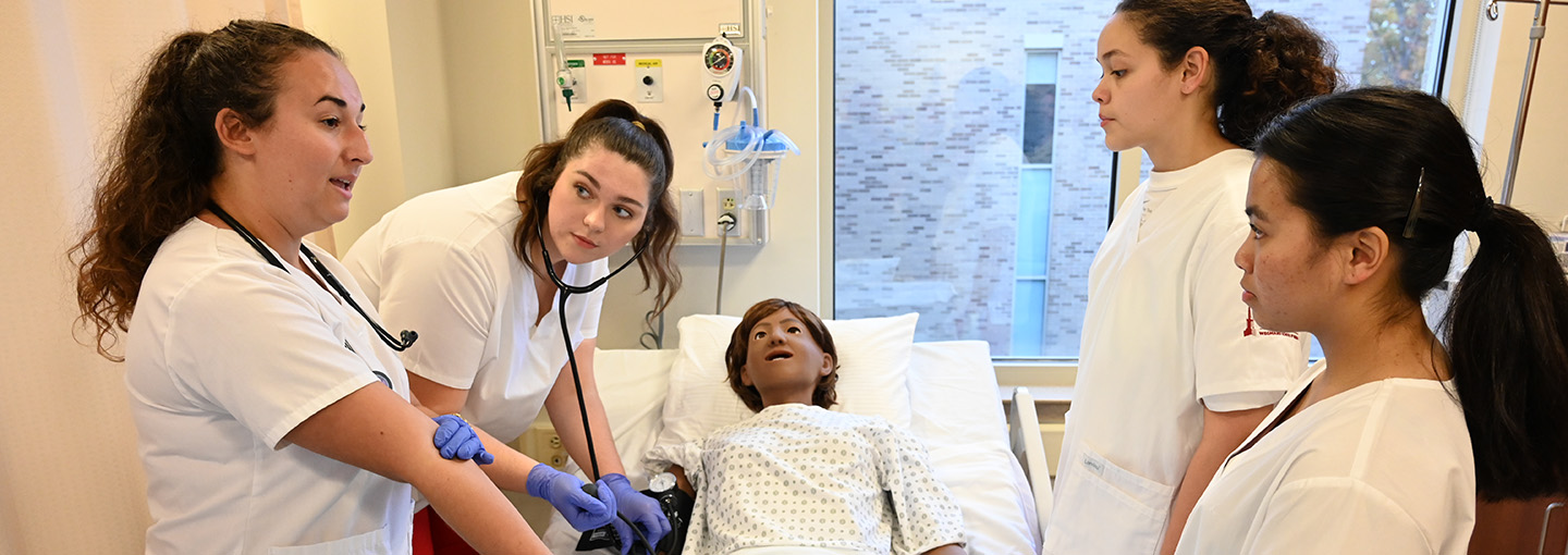 Four student nurses in simulated hospital setting caring for patient.