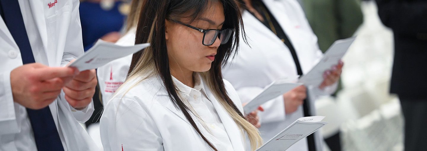 Pharmacy students in white coats taking the oath of a pharmacist.