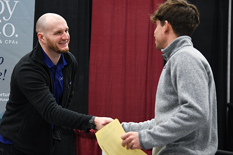 A student shakes hands with a company representative at a career fair.