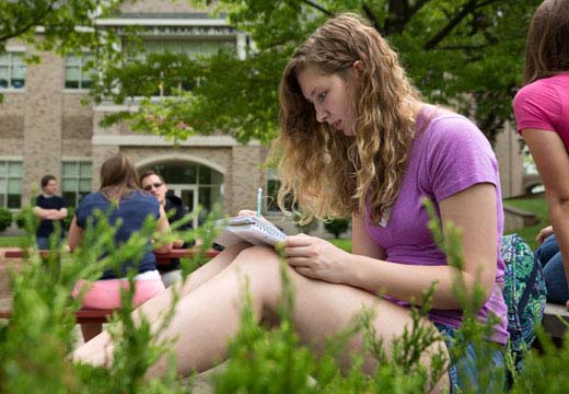 Student taking notes while sitting outside.