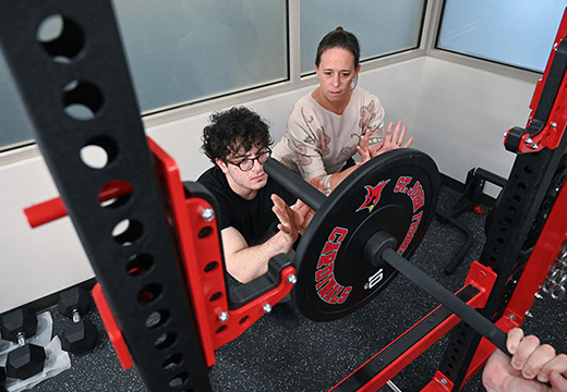 A professor models how to spot for a weightlifter in the athletic performance lab.