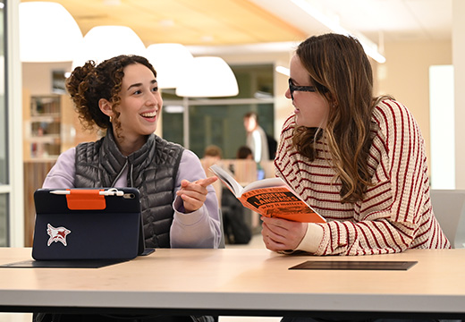 Students in Lavery Library discussing a book about modern languages.
